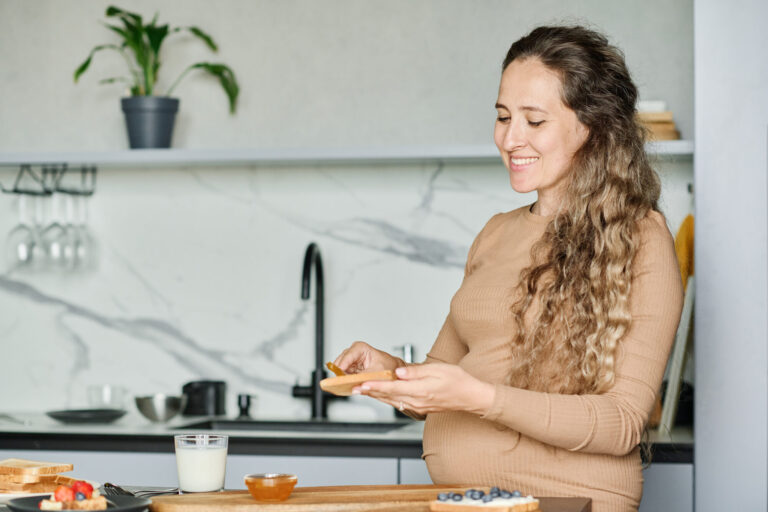 Femme enceinte souriante qui prépare une tartine dans une cuisine claire