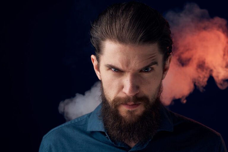 Homme barbu au regard furieux, sourcils froncés, avec de la fumée rougeâtre derrière la tête