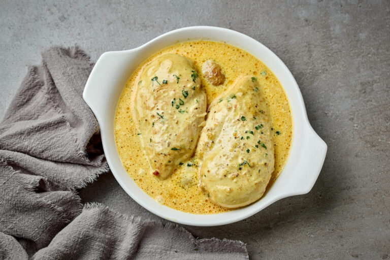 Deux blancs de poulet nappés d'une sauce crémeuse jaune parsemée d'herbes, dans un plat blanc