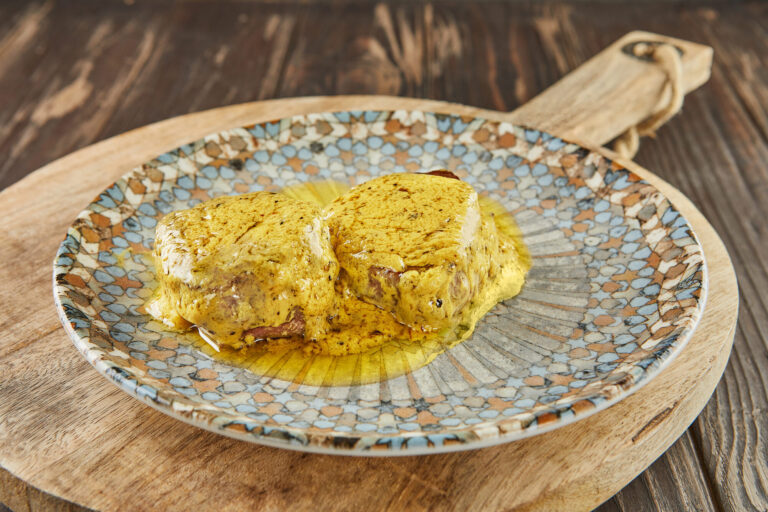 Médaillons de bœuf nappés d'une sauce à la moutarde jaune, servis sur une assiette à motifs posée sur une planche en bois