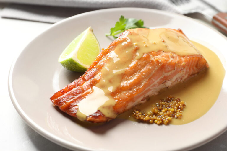 Pavé de saumon nappé de sauce à la moutarde, avec de la moutarde à l'ancienne et un quartier de citron vert sur une assiette