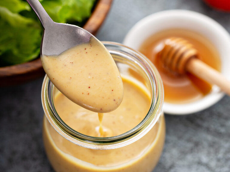 Cuillère de sauce miel-moutarde au-dessus d'un bocal en verre, à côté d'une coupelle de miel